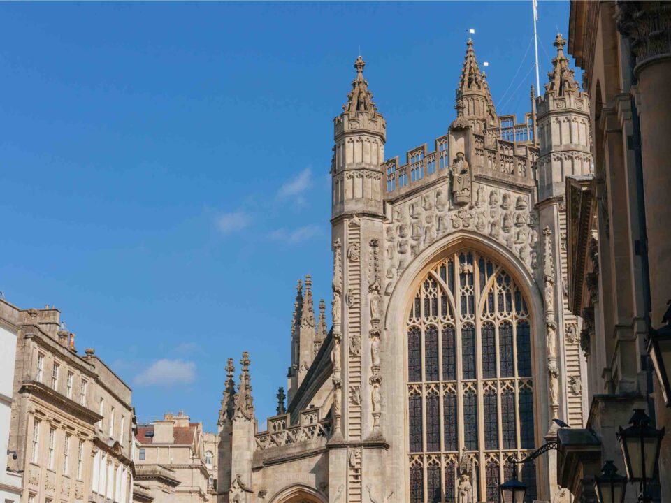 The upper part of Bath Abbey with surrounding buildings and blue sky