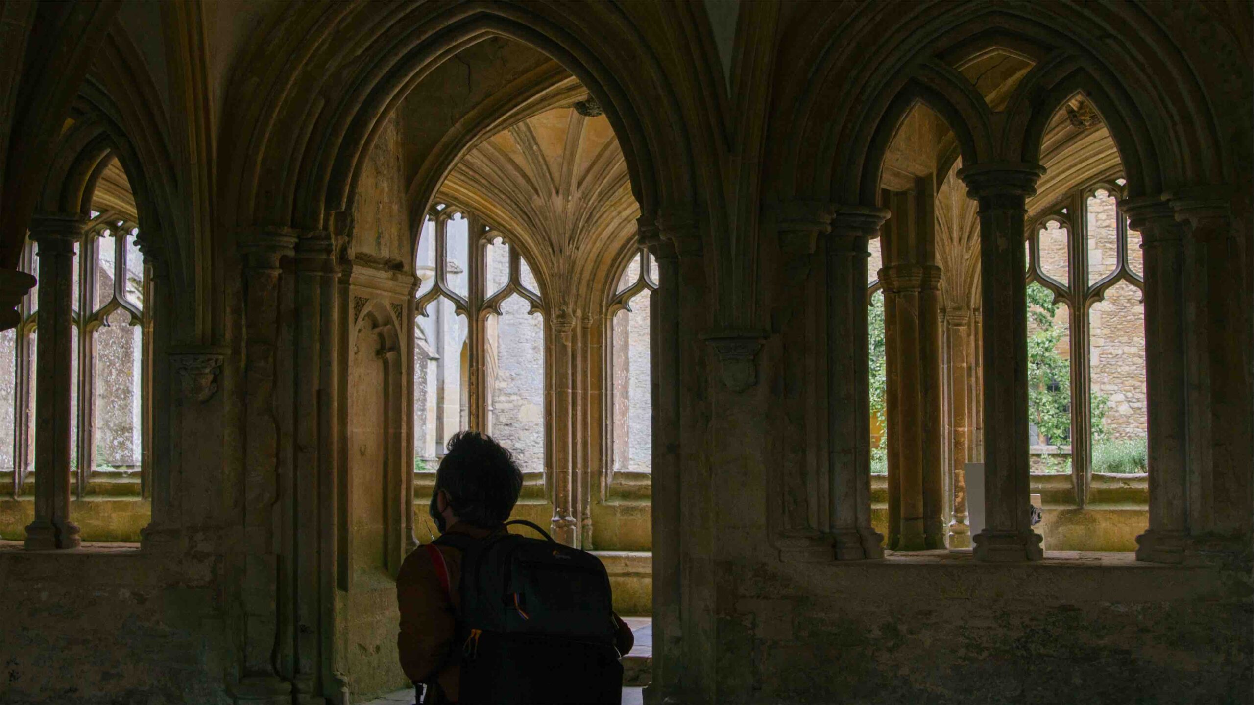 A man stands inside a building with tall cloisters.