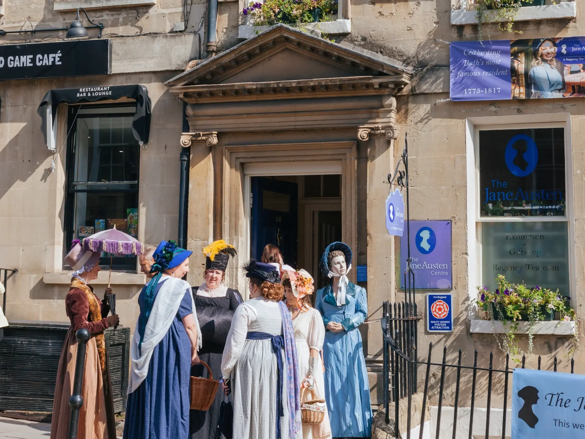5 women in period dress clothing stood outside the Jane Austen centre in Bath.