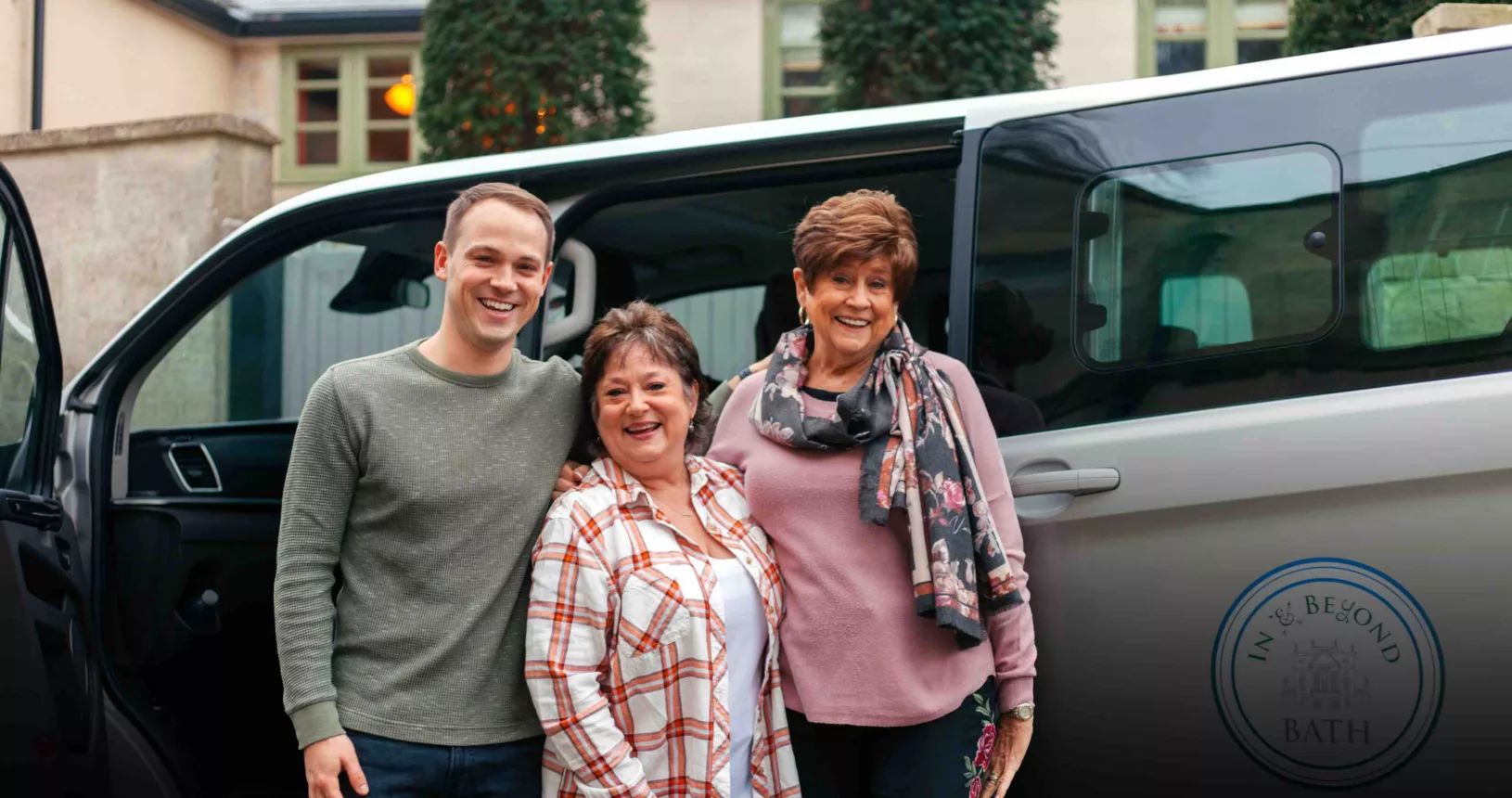 From left to right a man and two women stand in front of a van with the doors open