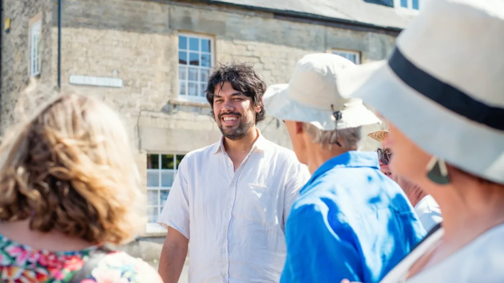 Tour guide Jules stands centre with guests around him on either side. In the background a Georgian building with glass windows makes a strong feature. A warm sunny day.