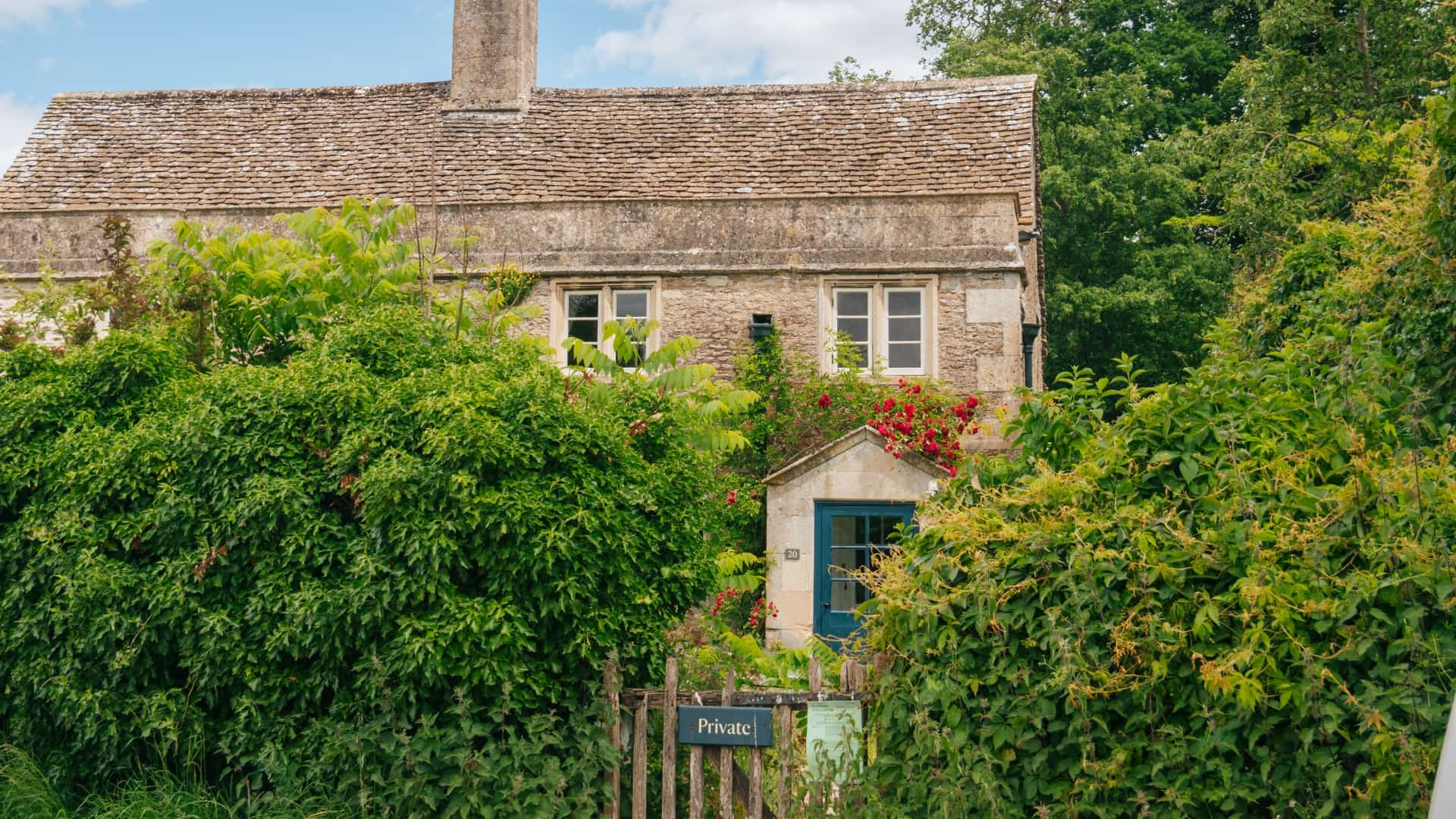 A traditional cottage with a thatched roof, surrounded by lush greenery and climbing vines. A small gate with a "Private" sign as this is a filming location for Harry Potter's childhood home, Godric's Hollow.