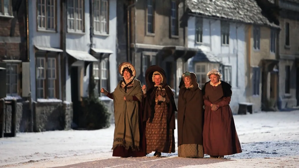 Four women walk along a snow covered street in period dress. This is Lacock village portrayed as Cranford Street in the Larkrise to Candleford production.