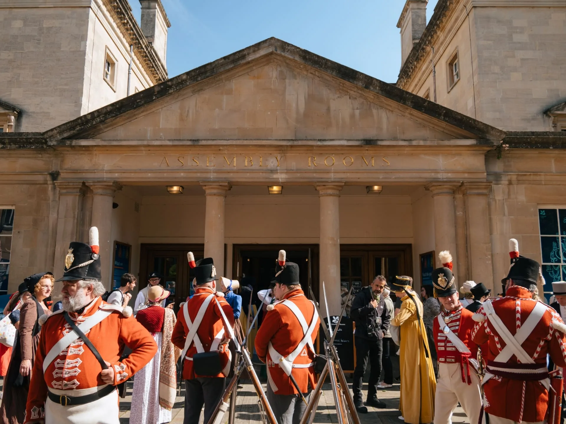 People in elegant Regency-era costumes gather outside the Bath Assembly Rooms, enjoying the festivities of the Jane Austen Festival.