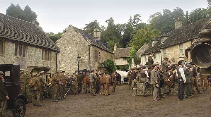 Actors in war-time period dress filming for War Horse in Castle Combe. The street is busy with extras and the road is covered with mud.