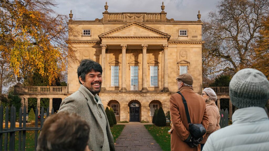 Jules Mittra, a tour guide from In & Beyond Bath, leads a group of guests outside the grand Georgian-style Holburne Museum. The building’s elegant columns stand against an autumnal backdrop, creating a warm and inviting scene, for a custom Walking Tour of Bath.