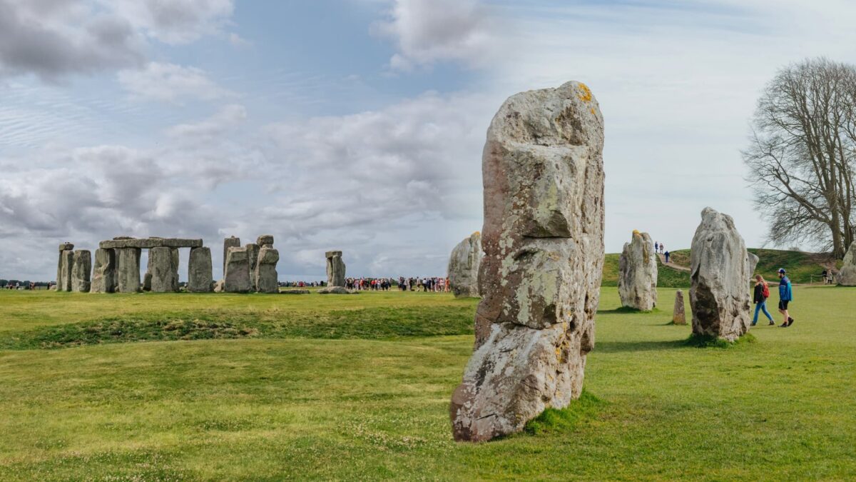 Avebury vs Stonehenge: A weathered sarsen stone at Avebury in the foreground with Stonehenge visible in the misty background, illustrating the contrast between the two ancient stone circles in Wiltshire